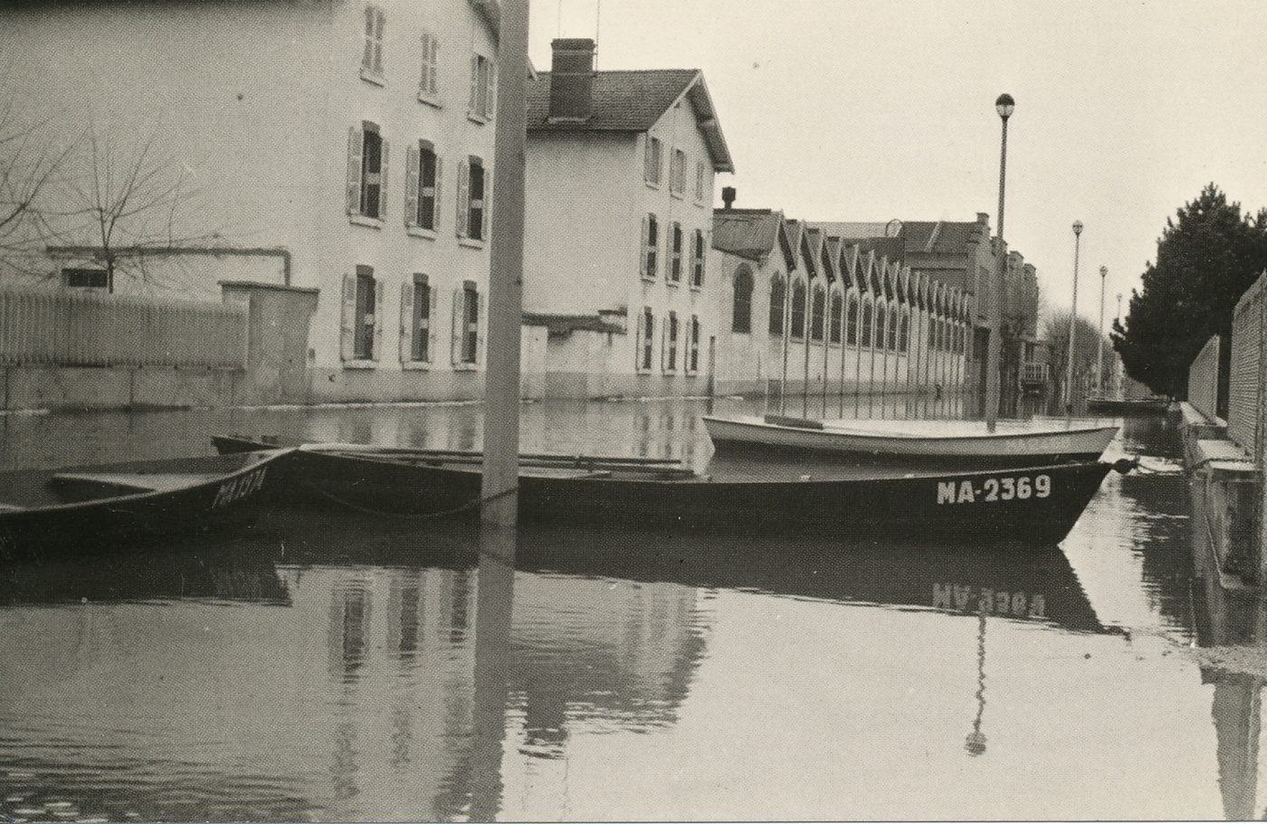 Mâcon. Crue de la Saône. Décembre 1981. Rue de la République. Toute la tristesse des jours et des soirs sans lumière, sans chauffage, de ce décembre 1981, pour des centaines de Mâconnais, s'exprime dans cette rue déserte, seulement peuplée de barques. Historique des crues. Principe de mesure des crues : le niveau zéro correspond à la cote 167,70 du nivellement général de la France et ne coincide donc pas nécessairement avec le fond variable de la rivière. Le niveau national de la Saône étant de 1,50 m au-dessus de ce zéro, il est aisé d'imaginer le volume d'eau retenu par le pont de Saint-Laurent, lorsque celle-ci s'élève au-dessus de 6 m.
