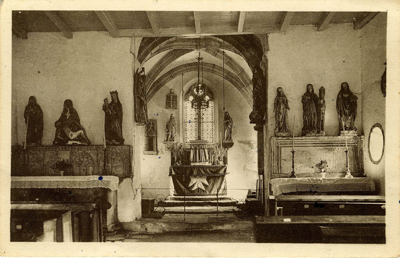 En Morvan, Uchon, Alt. 650 m. L'intérieur de l'église. Le maître-autel décoré d'un retable à arcatures gothiques finement ouvragées dans la pierre très dure. En avant-du-choeur : l'autel de gauche est dédié à la Vierge Marie ; l'autel de droite supporte les statues de sainte Barbe, sainte Madeleine et de sainte Geneviève.